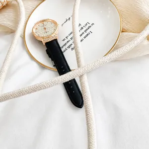 Détail d'une bandoulière tressée crème et d'une montre chic en or rose sur fond décoratif