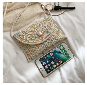 Détail d'une pochette en paille tressée avec broderie zigzag colorée et perle centrale