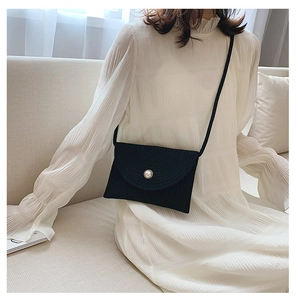 Détail d'un sac bandoulière noir en paille avec un fermoir en perle blanche sur mannequin