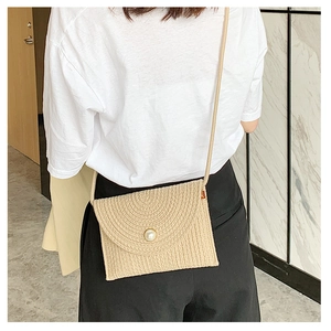 Détail d'un sac bandoulière en paille tissée beige avec bouton perle sur modèle