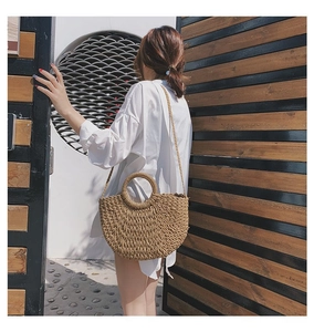 Détail d'un sac à bandoulière en paille tressée montrant la texture et les poignées rondes