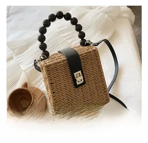 Close-up of woven straw handbag featuring black beaded handle and silver twist-lock