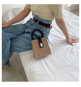 Straw handbag featuring unique black bead handle and metallic turn-lock closure detail
