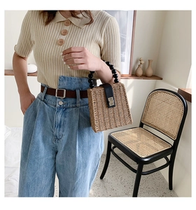 Detail of square straw handbag with black beaded handle and silver metal buckle lock