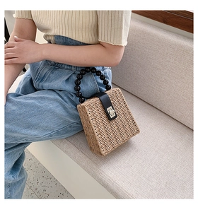 Close-up of straw woven tote bag featuring black beaded handles and metal twist lock