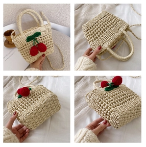 Detail view of woven straw beach bag featuring crochet cherry decor and dual handles