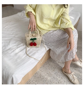 Detailed close-up of straw woven crossbody bag with red cherry charm on white background