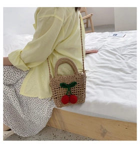 Detail of hand-woven straw crossbody bag with crochet cherry accents and round handle