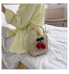 Detail of straw woven bag with 3D cherry pendants and white lining for summer beach style