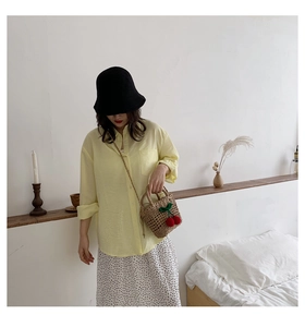 Detail of mini straw bag with cherry charm paired with yellow linen shirt and sun hat
