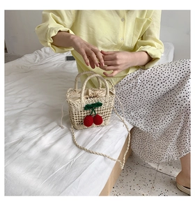 Detail of handmade straw mini bag with red cherry accents and a beige drawstring closure
