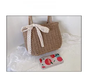 Straw handbag size comparison with phone featuring beige lace bow and natural finish
