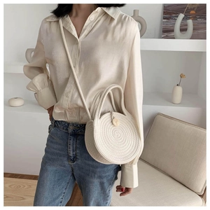 Detail of hand-woven cream round crossbody bag with wooden button and spiral texture