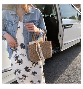 Detail of straw woven beach bag featuring a large white lace bow on the top handle