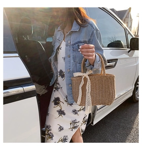Detail of straw woven handbag featuring elegant white lace bow on the handle
