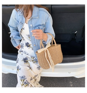 Close-up of straw tote bag with lace bow decoration shown in an outdoor lifestyle setting