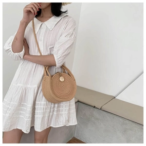 Detail of round straw crossbody bag featuring spiral weave and leather shoulder strap