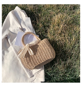Close-up of beige straw woven tote bag with a white lace bow on a grass background