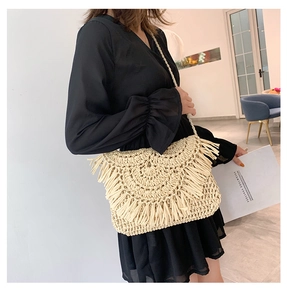 Beige woven straw crossbody bag with fringe detail and tassel flap on a summer dress