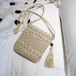Détail du sac bandoulière en paille avec texture florale ajourée et pompons à perles en bois