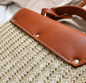 Dettaglio borsa di paglia con finiture in pelle marrone, cuciture bianche e rivetti metallici