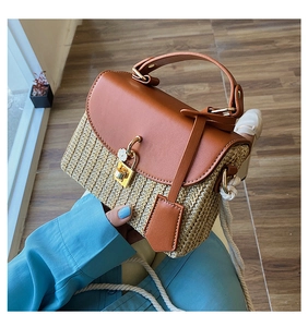 Dettaglio borsa in paglia con patta in pelle marrone e chiusura floreale in metallo