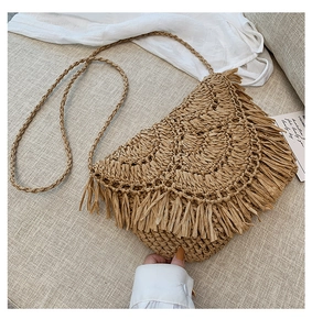 Close-up of handmade straw shoulder bag with long fringe tassels on beige fabric