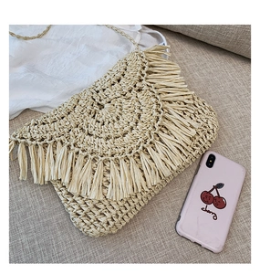 Flat lay of beige woven straw envelope bag with long fringes and bohemian details