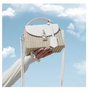 Detailed shot of straw woven square bag with white leather flap and golden metal clasp