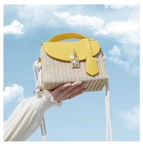 Detail of straw woven bag with yellow leather flap and white cotton rope strap on blue sky