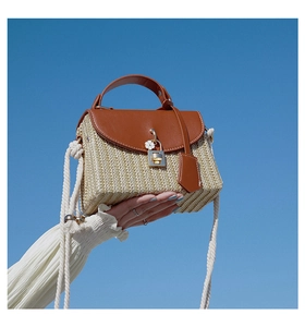 Detail of straw woven bag with brown leather lid and white flower charm on blue sky background