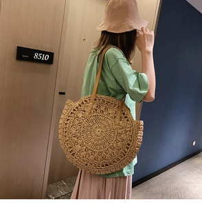 Side view of a large woven straw shoulder bag with brown leather straps for summer beach