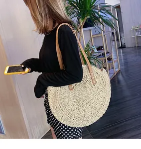 Model wearing a large round straw woven tote bag with brown leather handles for summer