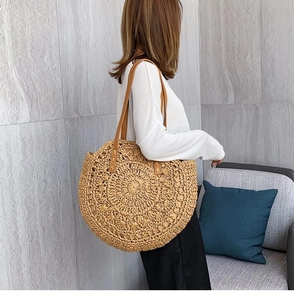 Detail of a round woven straw beach bag with brown leather straps on a model