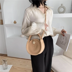 Handwoven round straw bag with dual handles and crossbody strap in natural beige tone