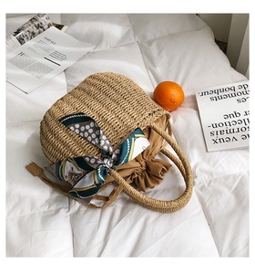 Dettaglio borsa in paglia con texture intrecciata naturale e foulard di seta decorativo