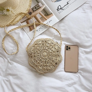 Detail of hand-woven beige straw crossbody bag with floral pattern on white linen