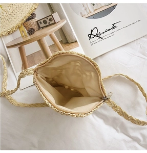 Detail view of beige woven straw bag with zipper closure, fabric lining and shoulder strap