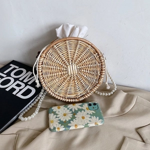 Sac bandoulière rond en paille avec chaîne perlée sur un blazer et magazine