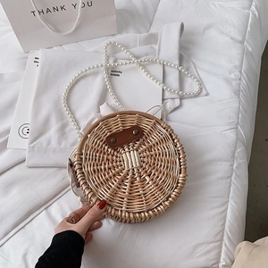 Détail d'un sac rond en paille tressée avec bandoulière en perles blanches et boucle cuir