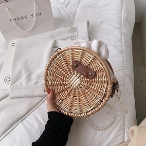 Détail du sac rond en paille avec chaîne en perles et accent en cuir sur le lit