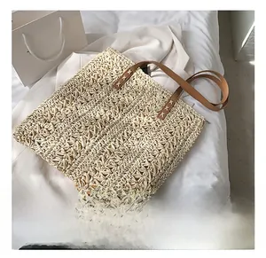 Close-up of woven straw tote bag featuring brown leather handles and cross-stitch detail