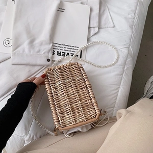 Détail d'un sac en rotin tressé main avec bandoulière en perles blanches sur tissu blanc