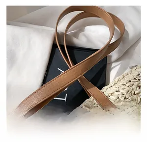 Detail view of woven straw tote bag with brown faux leather handles and cross-stitching