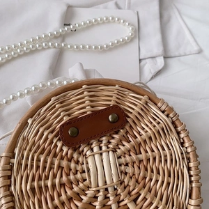 Détail d'un sac rond en paille avec bandoulière en perles et patch en cuir brun