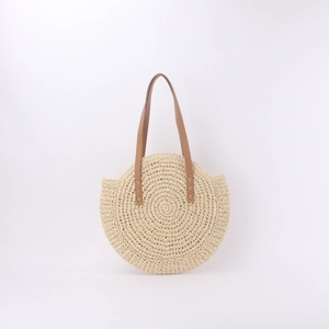Detail of hand-woven circular straw bag showing brown leather handles and stitch texture
