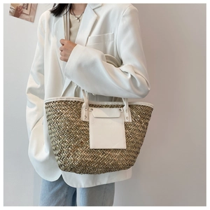 Close-up of woven straw tote bag featuring white leather pocket and shoulder strap details