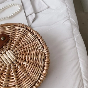 Détail d'un sac rond en rotin fait main avec lanière en cuir, rivets et perles