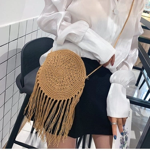 Detail of round straw crossbody bag featuring long tassels and woven texture