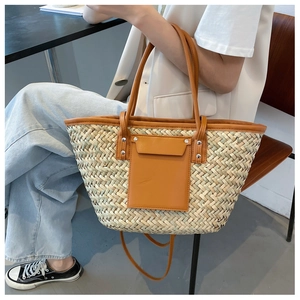 Detail of woven straw tote bag featuring caramel leather pocket and metal rivets